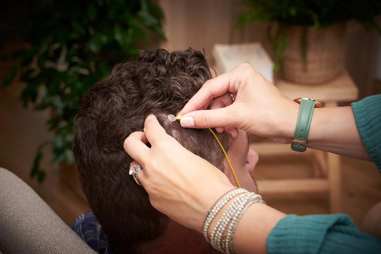 La praticienne pose un capteur de neurofeedback sur le cuir chevelu d'un client